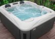 Un jacuzzi bouillonnant aux bords blancs trône sur une terrasse en bois, entouré de verdure et de plantes, créant ainsi une oasis de sérénité qui rappelle les piscines de luxe.