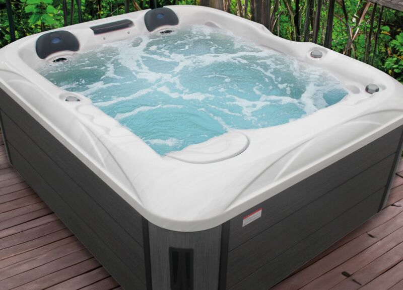 Un jacuzzi bouillonnant aux bords blancs trône sur une terrasse en bois, entouré de verdure et de plantes, créant ainsi une oasis de sérénité qui rappelle les piscines de luxe.