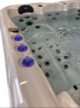 Gros plan sur un jacuzzi doté de plusieurs jets et de trois fontaines éclairées de bleu dont les jets dessinent des arcs au-dessus de l'eau bouillonnante. L'intérieur est de couleur claire et l'eau est limpide, avec de légères ondulations.