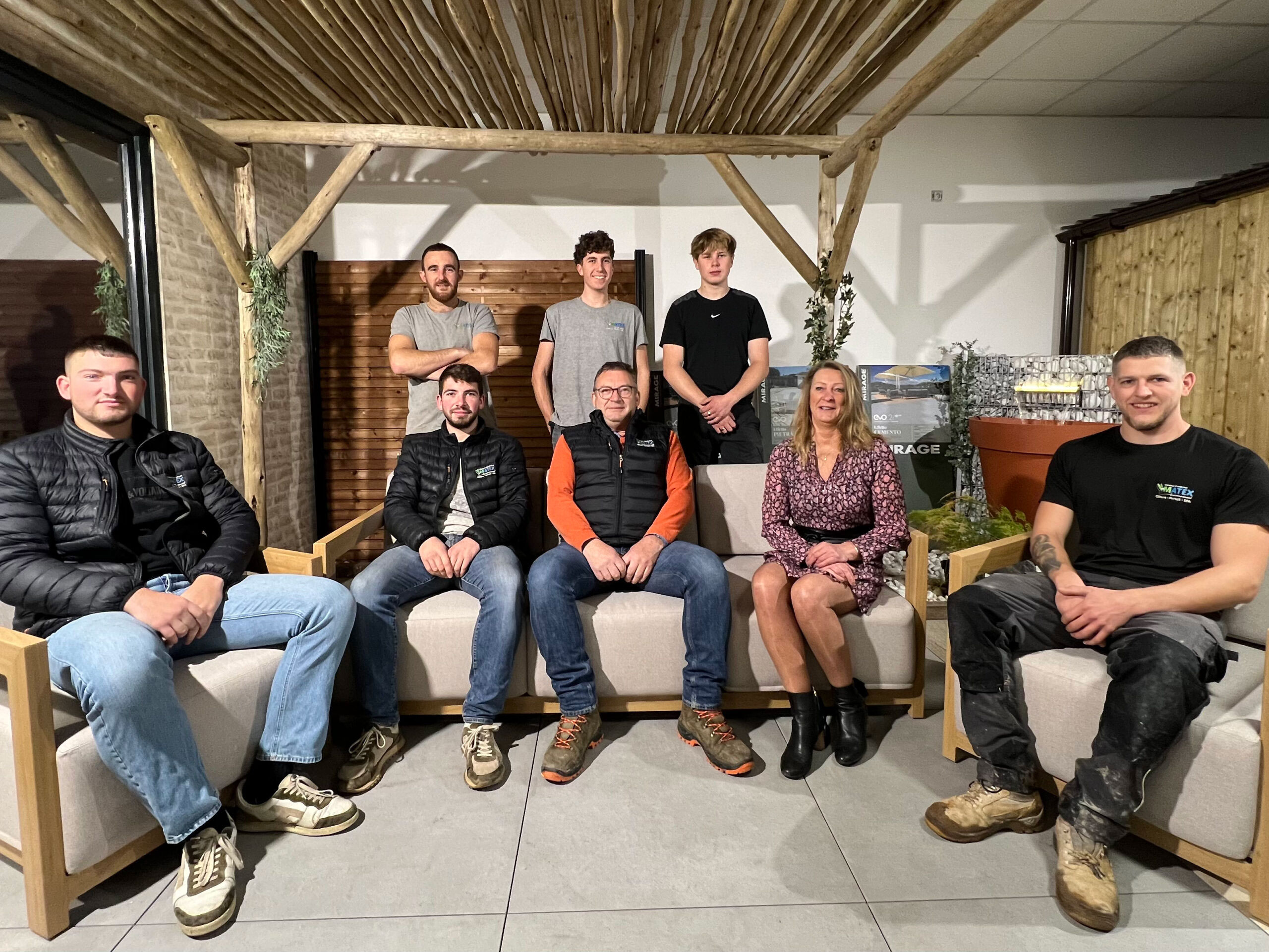 Un groupe de sept personnes posant pour une photo dans un showroom : trois d'entre elles se tiennent debout derrière un canapé et quatre sont assises dessus.